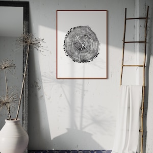 Puede incluir: Una impresión en blanco y negro de un patrón de anillos de árbol en un marco marrón que cuelga de una pared blanca con un paño blanco drapeado sobre una escalera de madera.