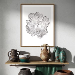 May include: A framed black and white print of a stylized flower design hangs above a wooden shelf with a collection of rustic pottery. The pottery includes a teal-colored vase, a brown vase, and a brown and teal bowl.