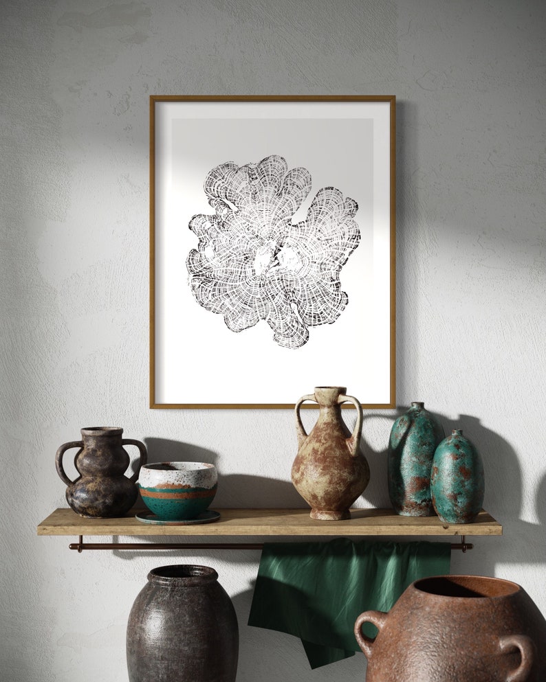 May include: A framed black and white print of a stylized flower design hangs above a wooden shelf with a collection of rustic pottery. The pottery includes a teal-colored vase, a brown vase, and a brown and teal bowl.