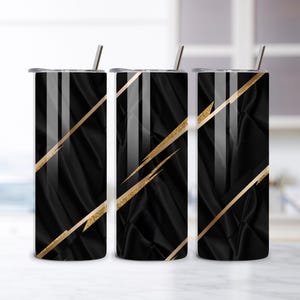 Può includere: Tre bicchieri neri in acciaio inossidabile con strisce diagonali dorate e un coperchio nero. Ogni bicchiere ha una cannuccia argentata. I bicchieri sono cilindrici e hanno un aspetto strutturato simile al tessuto.