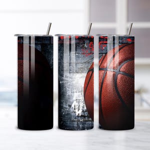 Puede incluir: Tres vasos de acero inoxidable con diseños de baloncesto. Los diseños presentan una pelota de baloncesto, un fondo oscuro y un fondo de estilo grunge. Cada vaso tiene una pajita plateada y una tapa.
