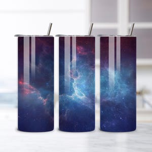 May include: Three stainless steel tumblers with a space-themed design. The tumblers feature a vibrant nebula pattern in shades of blue, purple, and red. Each tumbler has a silver lid and a matching straw, perfect for cold beverages.