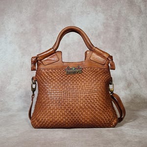 Peut inclure: Sac &agrave; main en cuir marron avec un motif tiss&eacute;. Le sac a une poign&eacute;e sup&eacute;rieure et une bandouli&egrave;re amovible. Un fermoir d&eacute;coratif avec des pierres color&eacute;es est centr&eacute; sur le devant.