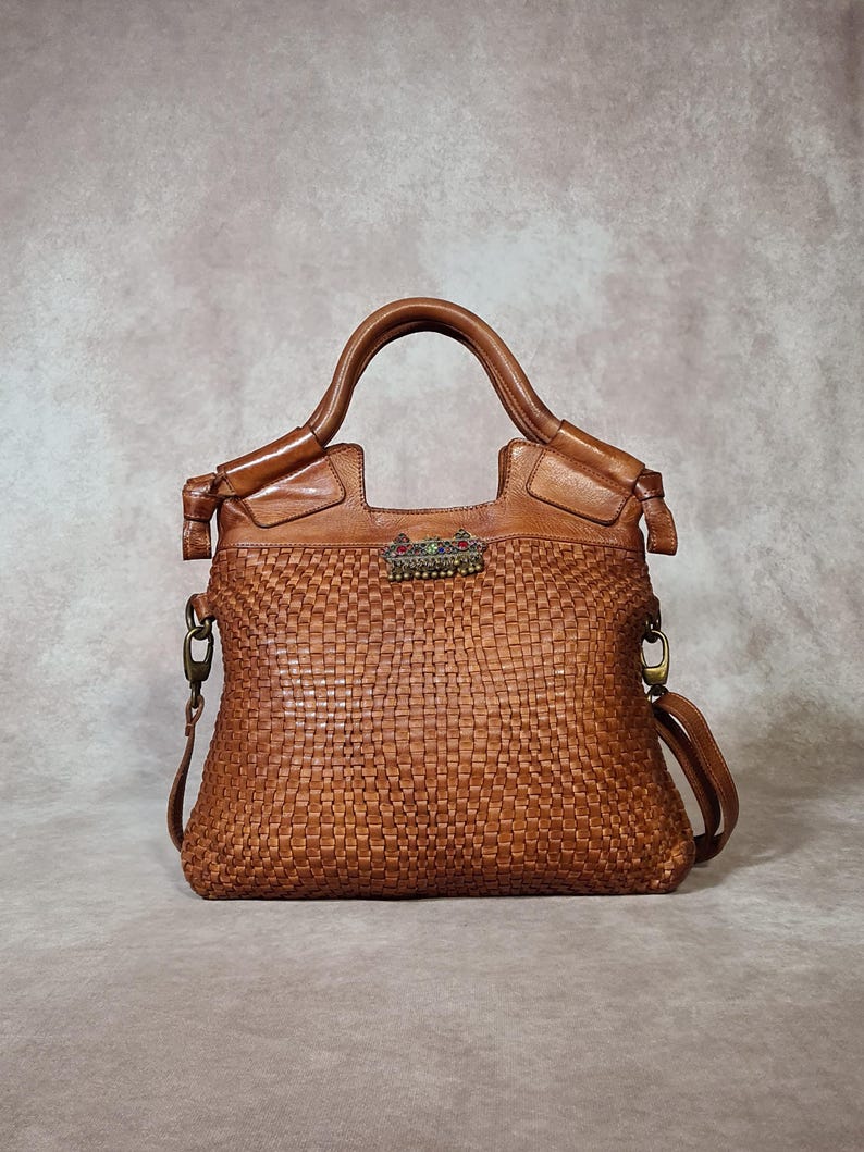 Peut inclure: Sac &agrave; main en cuir marron avec un motif tiss&eacute;. Le sac a une poign&eacute;e sup&eacute;rieure et une bandouli&egrave;re amovible. Un fermoir d&eacute;coratif avec des pierres color&eacute;es est centr&eacute; sur le devant.