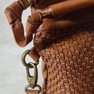 Peut inclure: Gros plan sur un sac &agrave; main en cuir marron avec un motif tiss&eacute;. Le sac est dot&eacute; d'une poign&eacute;e robuste et d'une bandouli&egrave;re amovible avec un fermoir en m&eacute;tal. Le cuir a un aspect riche et textur&eacute;.