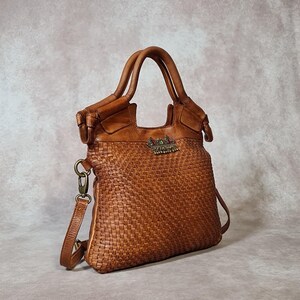 Peut inclure: Un sac &agrave; main en cuir marron avec un motif tiss&eacute;. Le sac poss&egrave;de deux poign&eacute;es et une bandouli&egrave;re amovible. Un embl&egrave;me d&eacute;coratif en m&eacute;tal est pr&eacute;sent sur le devant. Le sac est en cuir et a un look classique et intemporel.