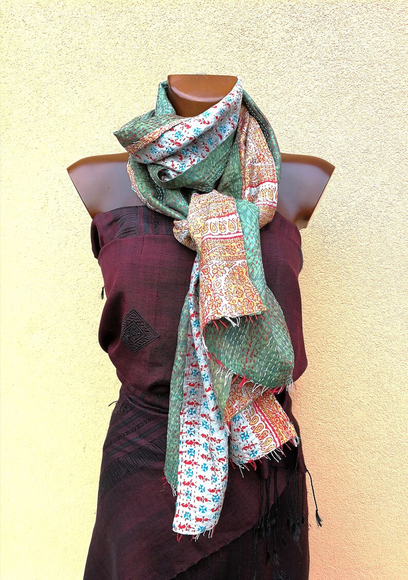 May include: A colorful scarf with a patchwork design, featuring green, white, and red patterns. The scarf is draped over a mannequin, showcasing its intricate stitching and vibrant colors. The scarf's design includes floral and geometric motifs.