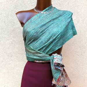 May include: A teal and brown patterned wrap is draped over a mannequin, paired with a burgundy skirt. The wrap is secured at the waist, with a fringed edge revealing a colorful paisley design. A silver necklace adorns the mannequin's neck.