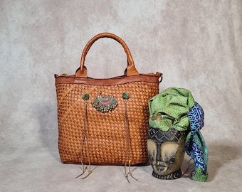Sac cabas artisanal en cuir tressé couleur cognac, orné de motifs ethniques Kuchi, de franges et de pompons. Pièce unique de style bohème avec bandoulière.