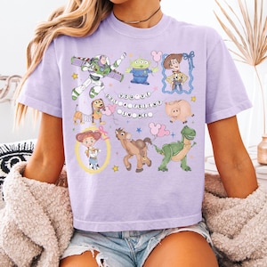 Puede incluir: Camiseta lila claro con personajes de dibujos animados de Toy Story. La camiseta muestra la frase "You've got a friend in me". Los personajes incluyen a Buzz Lightyear, Woody y los pequeños hombres verdes.
