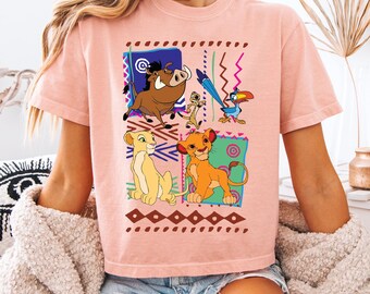 May include: A light pink t-shirt featuring a colorful graphic of characters from The Lion King. The design includes Simba, Nala, Timon, Pumbaa, and Zazu, set against a geometric background. The shirt is made of a soft material.