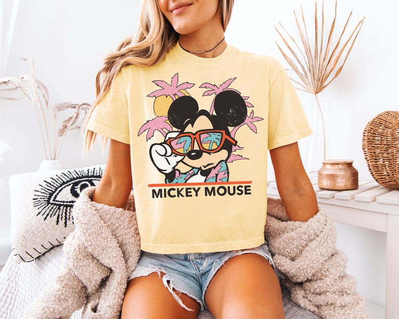 May include: Yellow t-shirt featuring Mickey Mouse wearing sunglasses with a tropical scene reflected in the lenses. The graphic includes palm trees, a sun, and the text "MICKEY MOUSE" in red.