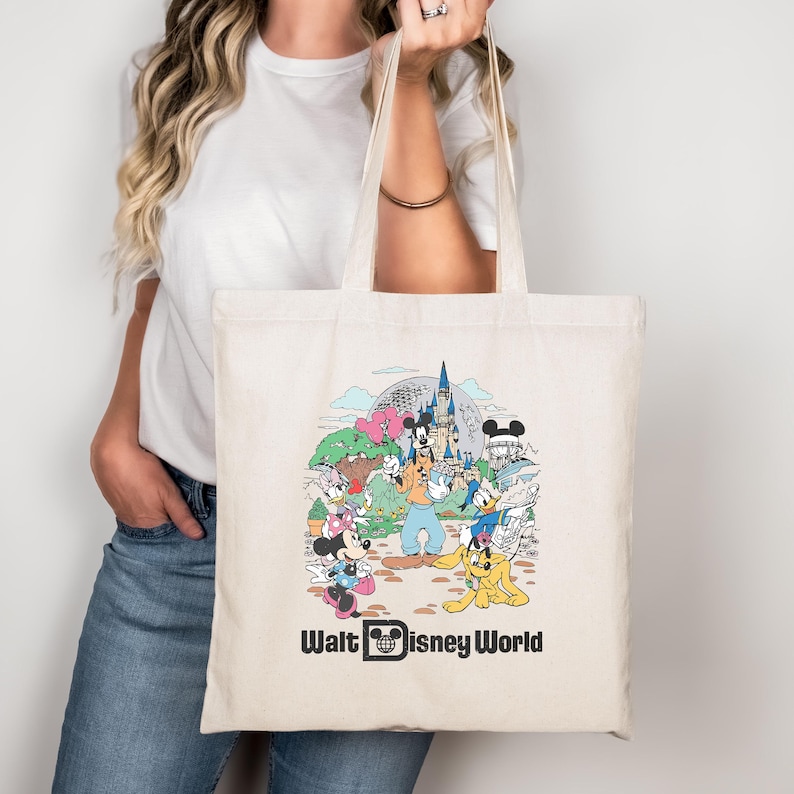 May include: Cream-colored tote bag featuring a colorful illustration of Disney characters and landmarks. The design includes Mickey Mouse, Minnie Mouse, Goofy, Donald Duck, and a castle. The words "Walt Disney World" are printed at the bottom.