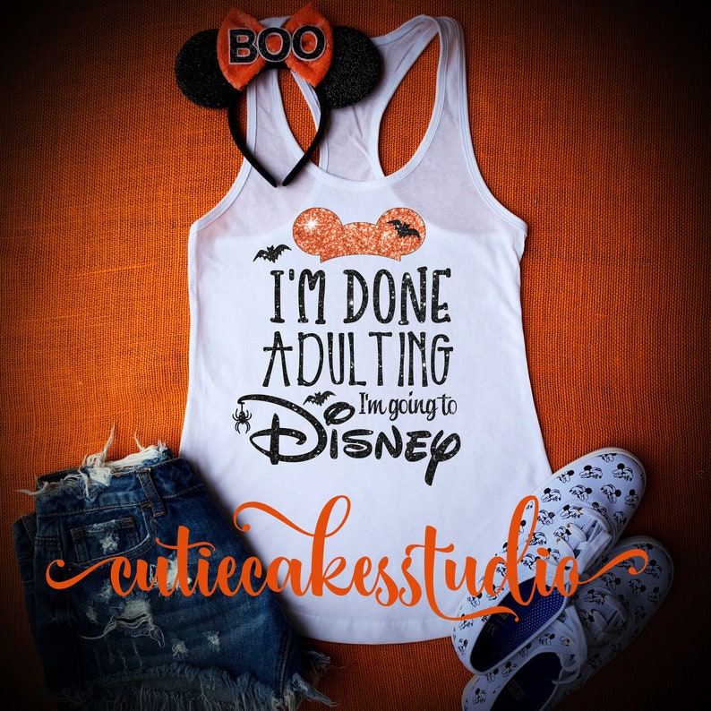May include: White tank top with a black and orange graphic that says "I'm Done Adulting I'm going to Disney" with a black and orange Mickey Mouse head above the text. The tank top is on a orange background with a pair of black mouse ears with an orange bow that says "BOO" on them.