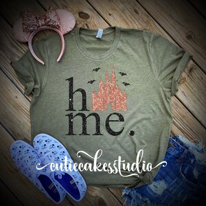 May include: A green t-shirt with the text "home" and a glittery pink castle graphic. The castle is surrounded by bats. The text "cutiecakesstudio" is written in cursive at the bottom of the shirt.
