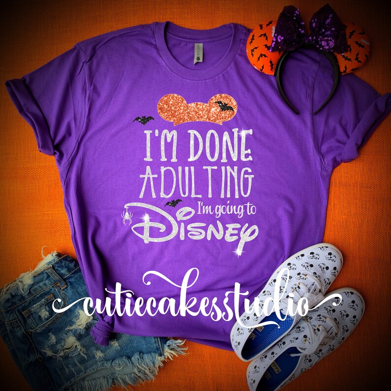 May include: Purple t-shirt with glitter text that reads "I'm done adulting I'm going to Disney" with a glittery orange Mickey Mouse ear on the top left corner.