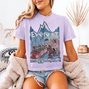 May include: A light purple t-shirt featuring a graphic of the Expedition Everest ride at Walt Disney World. The design includes the word "Everest" above a cartoon scene with Mickey Mouse and friends. The Walt Disney World logo is at the bottom.
