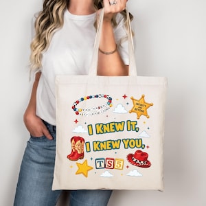 Może przedstawiać: Beżowa torba pł&oacute;cienna z kolorowym nadrukiem graficznym. Wz&oacute;r zawiera bransoletkę z koralik&oacute;w z napisem "You've got a friend in me", ż&oacute;łtą gwiazdę szeryfa, czerwone kowbojki, czerwony kapelusz oraz napis "I KNEW IT, I KNEW YOU, TS5".
