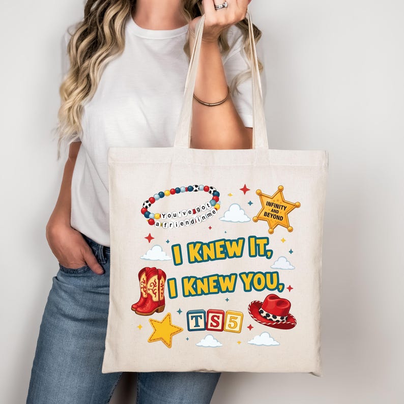 Może przedstawiać: Beżowa torba pł&oacute;cienna z kolorowym nadrukiem graficznym. Wz&oacute;r zawiera bransoletkę z koralik&oacute;w z napisem "You've got a friend in me", ż&oacute;łtą gwiazdę szeryfa, czerwone kowbojki, czerwony kapelusz oraz napis "I KNEW IT, I KNEW YOU, TS5".