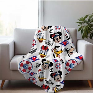 May include: White Disney-themed blanket featuring Mickey Mouse, Minnie Mouse, Donald Duck, Daisy Duck, and Goofy. The blanket has a repeating pattern of Disney characters, anchors, and life preservers with the text "Disney Wish".