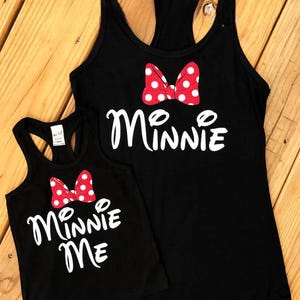 May include: Two black tank tops with white text and a red bow with white polka dots. The larger tank top says "Minnie" and the smaller tank top says "Minnie Me".