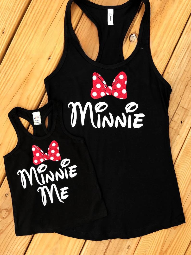 May include: Two black tank tops with white text and a red bow with white polka dots. The larger tank top says "Minnie" and the smaller tank top says "Minnie Me".