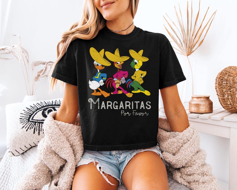 Op de afbeelding: Zwart T-shirt met drie stripfiguren met sombrero's. De tekst "Margaritas Por Favor" is wit. De karakters zijn geel, blauw, groen en roze.