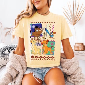 May include: Yellow t-shirt featuring a colorful graphic of characters from The Lion King. The design includes Simba, Nala, Timon, Pumbaa, and Zazu, set against a geometric background. The shirt is a casual, short-sleeved style.