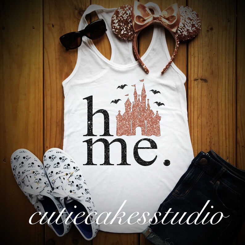 May include: White tank top with a black graphic that says "home" with a rose gold glitter castle and bats. The castle is a silhouette of the Cinderella Castle at Walt Disney World.
