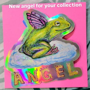 May include: A holographic sticker featuring a green frog with pink and purple wings, perched on a cloud. The word "ANGEL" is written in gold letters below the frog. The text "New angel for your collection" is at the top.