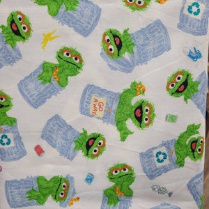 May include: White fabric with a repeating pattern of green Sesame Street character, Oscar the Grouch, holding a blue bin. The bin has a recycle symbol on it. The fabric also has a yellow lightning bolt and a red can.
