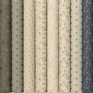 May include: A collection of rolled fabric bolts in various shades of blue, gray, and beige. The fabrics feature floral, paisley, and geometric patterns. The bolts are arranged side by side, showcasing the variety of designs and colors.