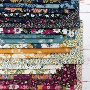May include: A stack of fabric swatches featuring various floral patterns in shades of blue, pink, yellow, and green. The fabrics are neatly folded, showcasing a variety of designs, including small and large floral prints. The image is well-lit, highlighting the textures and colors.