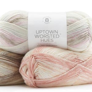 May include: Three skeins of Uptown Worsted Hues yarn in shades of pink, beige, and brown. The yarn is a variegated blend of colors.