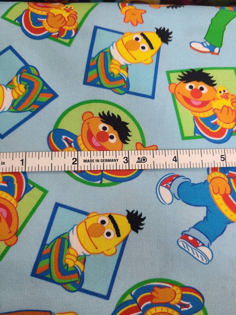 May include: Blue fabric with a repeating pattern of Sesame Street's Big Bird. Big Bird is wearing a blue and green striped shirt and has a yellow face with a black eyebrow. The fabric is 12.7 cm wide.