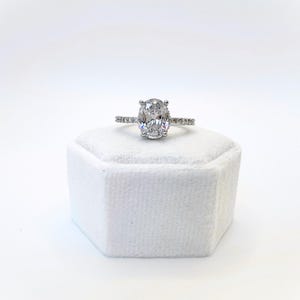 Peut inclure: Une bague en argent avec une grande pierre ovale transparente et de plus petites pierres transparentes serties dans la bande.