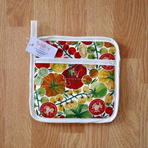 May include: White cotton pot holder with a red, yellow and green tomato print. The pot holder has a white border and a small tag that says "Rachellew Designs".