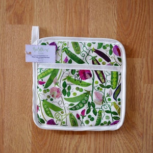 Puede incluir: Un agarrador de olla cuadrado con borde blanco y lazo para colgar. La tela presenta un estampado de vainas de guisantes verdes, flores moradas y hojas sobre fondo blanco. La etiqueta dice "Peas, Pods & Petals Pot Grab".