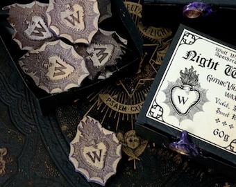 Peut inclure: Une boîte noire avec une étiquette blanche qui indique "Night Wing Gothic Victoria Wax Melt Violet, Musk, Sweet Rose 60g". La boîte contient une fonte de cire en forme de cœur avec un "W" au centre. La boîte est entourée de plusieurs autres fontes de cire en forme de cœur avec un "W" au centre.