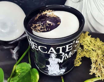 May include: Black candle jar with a white crescent moon design and the text "Hecate's Moon" on the front. The candle jar is filled with a purple wax and dried herbs.