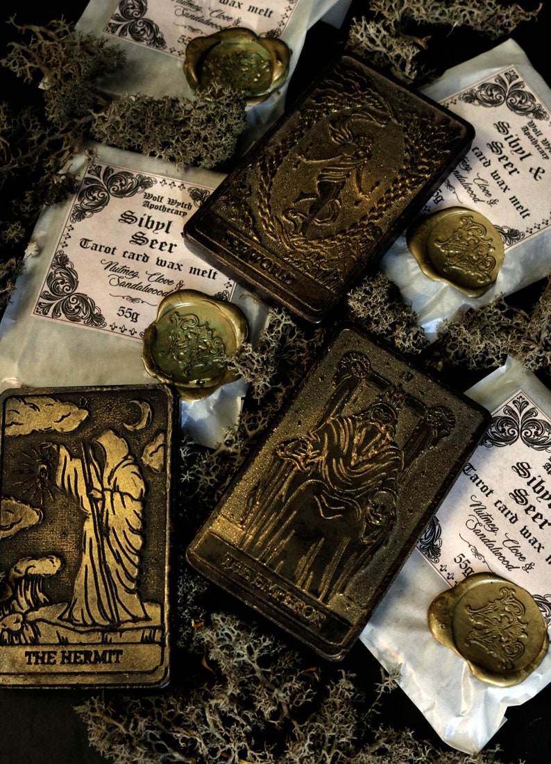 May include: Four tarot card wax melts with gold foil accents and wax seals. The cards are The Hermit, The Empress, The World, and Sibyl Seer. The wax melts are packaged in white paper with black text and are labeled with the card name, scent, and weight.
