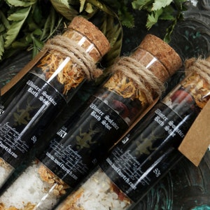 May include: Three glass test tubes filled with bath salts and dried herbs, labeled "Winter Solstice Bath Shot". The tubes are tied with twine and have cork stoppers.