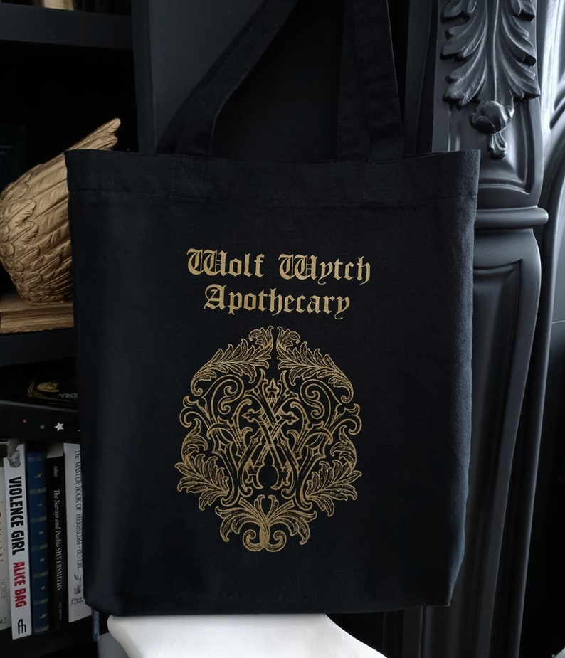 May include: Black tote bag with gold lettering that reads "Wolf Wytch Apothecary". A gold ornate design is centered on the bag.