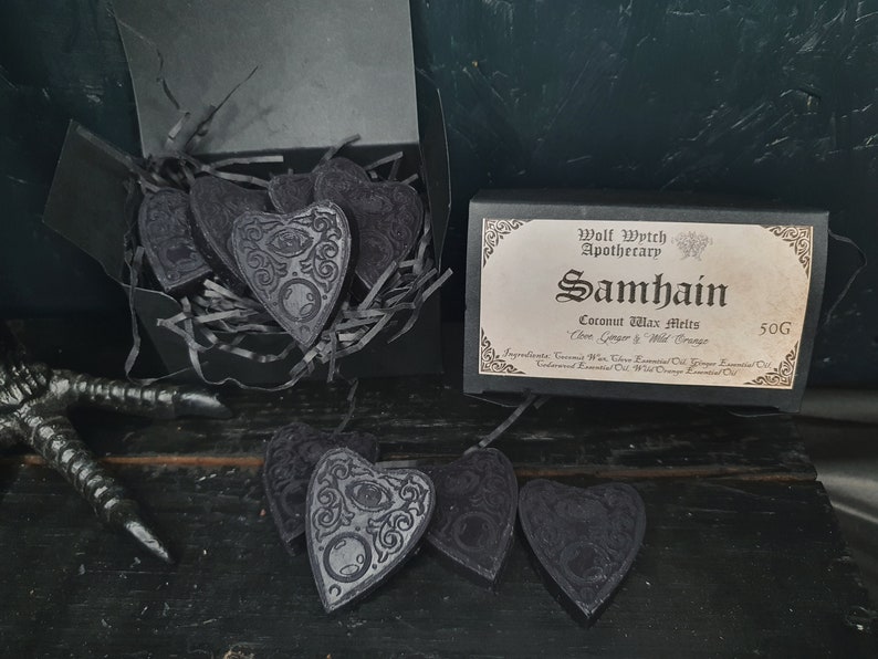 May include: A black box with a label that reads "Wolf Wytch Apothecary Samhain Coconut Wax Melts 50G  Clove, Ginger & Wild Orange"  The box contains six black heart-shaped wax melts with a decorative design.