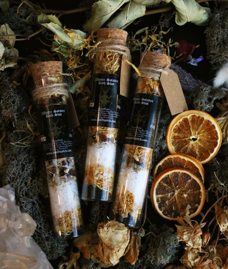 May include: Three small glass bottles filled with bath salts and dried flowers. The bottles have cork stoppers and are labeled "Winter Solstice Bath Shot".
