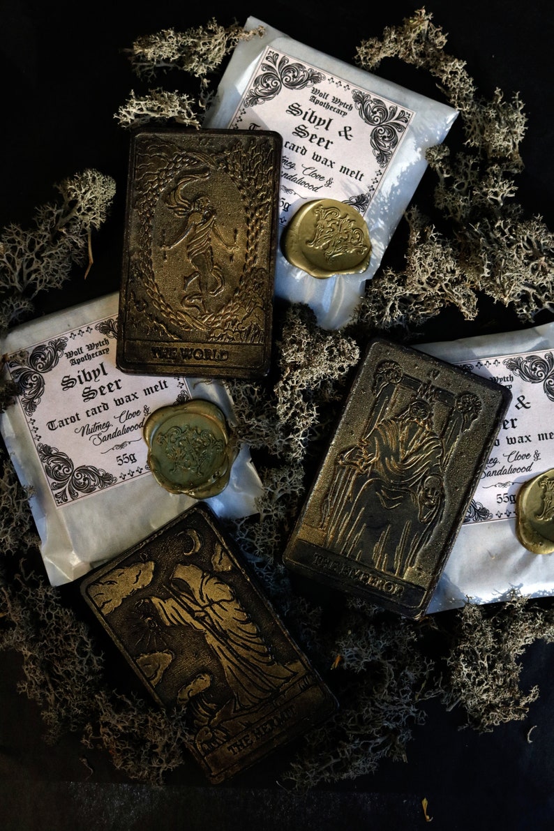 May include: Four tarot card wax melts with gold foil accents and a black background. The cards are labeled "The World", "The Hermit", "Sibyl & Seer", and "Sibyl & Seer". Each card has a wax seal with a gold design.