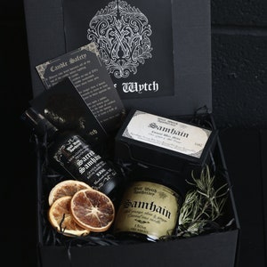 May include: A black gift box filled with a black and gold candle, a bottle of essential oil, and a bag of wax melts. The candle and oil are labeled "Samhain" and the wax melts are labeled "Samhain Coconut Wax Melts".