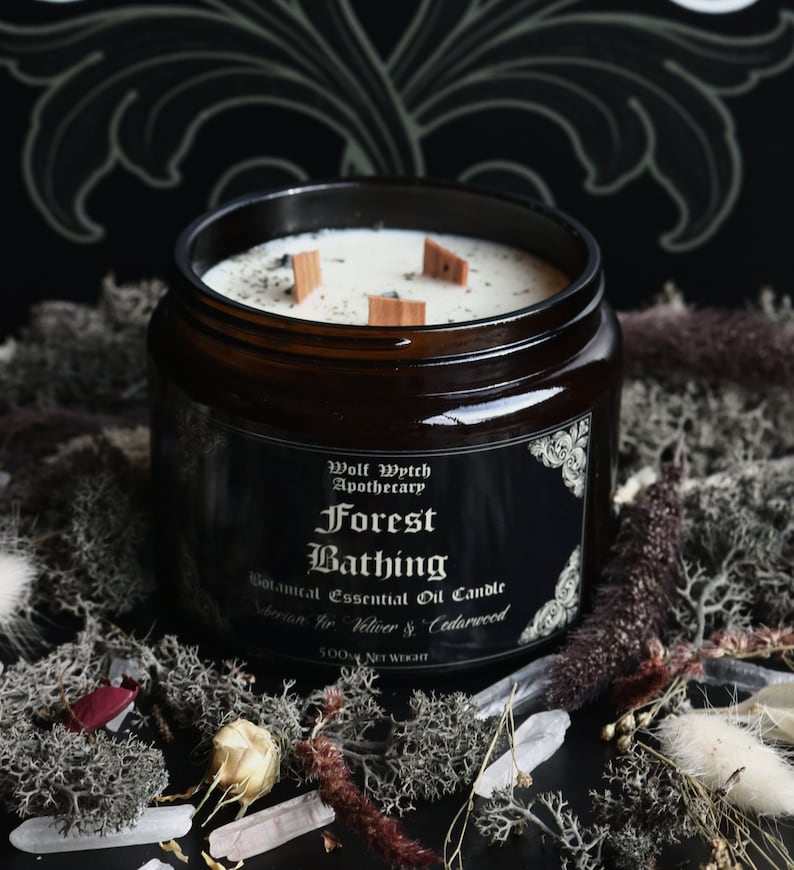 K&ouml;nnte beinhalten: Eine dunkelbraune Glasgef&auml;&szlig;kerze mit einem schwarzen Etikett, auf dem "Wolf Wytch Apothecary Forest Bathing Botanical Essential Oil Candle Siberian Fir, Vetiver & Cedarwood 500g NET WEIGHT" steht. Die Kerze hat einen wei&szlig;en Wachsoberteil mit drei Holzdochten.