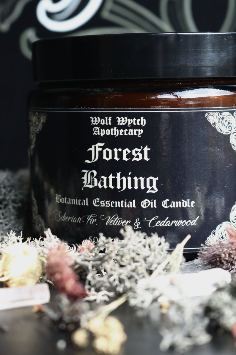 K&ouml;nnte beinhalten: Ein schwarzes Glasgef&auml;&szlig; mit einem wei&szlig;en Etikett, auf dem "Wolf Wytch Apothecary Forest Bathing Botanical Essential Oil Candle Siberian Fir. Vetiver & Cedarwood" steht.