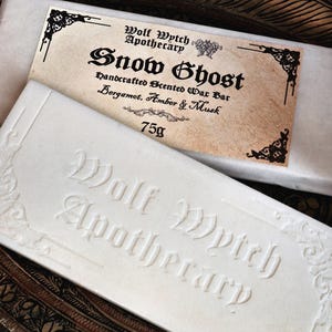 K&ouml;nnte beinhalten: Eine wei&szlig;e Seife mit dem gepr&auml;gten Text "Wolf Wytch Apothecary" und einem Etikett mit der Aufschrift "Snow Ghost" mit Duftdetails. Die Seife wiegt 75g.